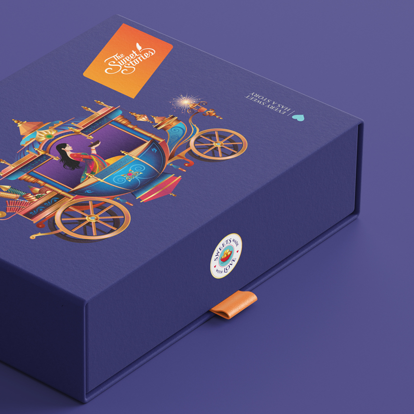 Sweet Stories Diwali Special Edition gift 
              box with vibrant illustration of a royal festive carriage, a traditional Indian woman, sparkling diya elements, and a purple theme representing celebration and storytelling. 
              Includes logo, orange ribbon pull, and 'Sweets made with love' seal.