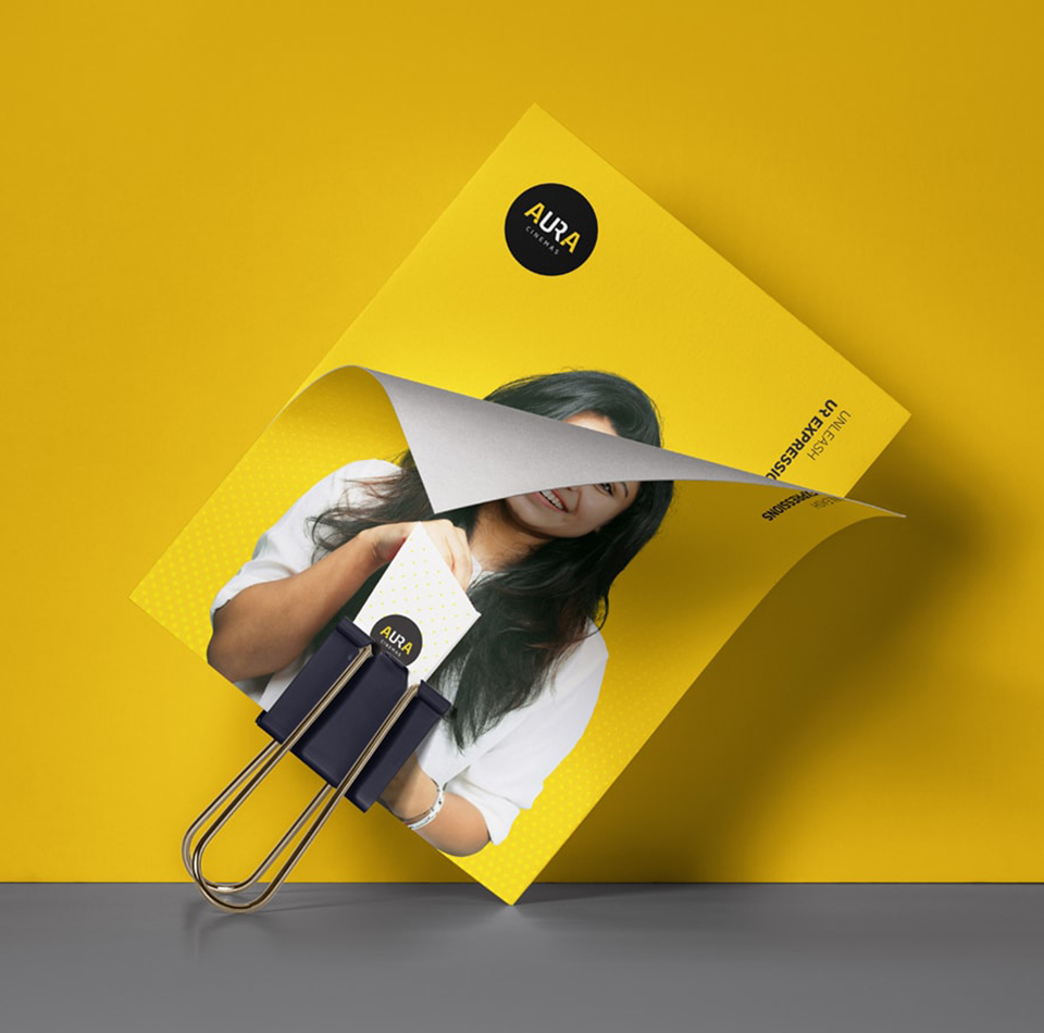 Aura Cinemas cinema experience: Flyer showcasing a happy moviegoer with a ticket and brand messaging on a vibrant yellow backdrop.