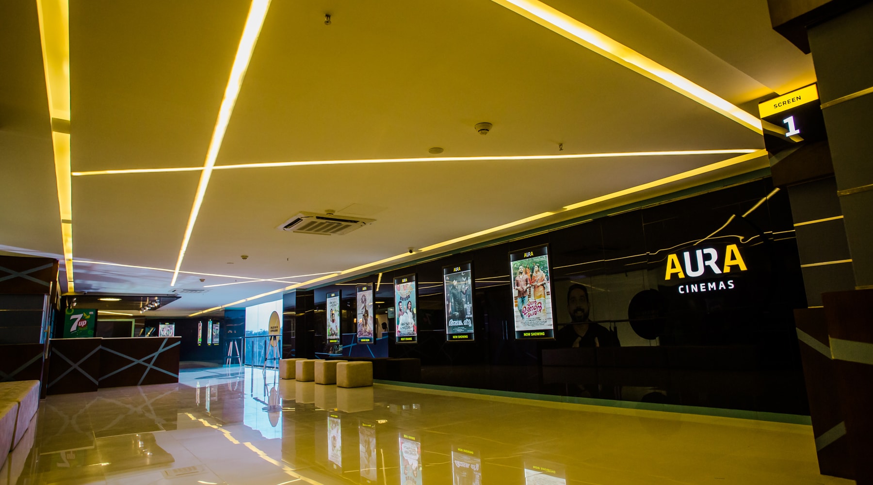 Aura Cinemas multiplex interior: View of the concession stand, glowing ceiling lights, and current movie posters, offering a welcoming atmosphere for moviegoers.