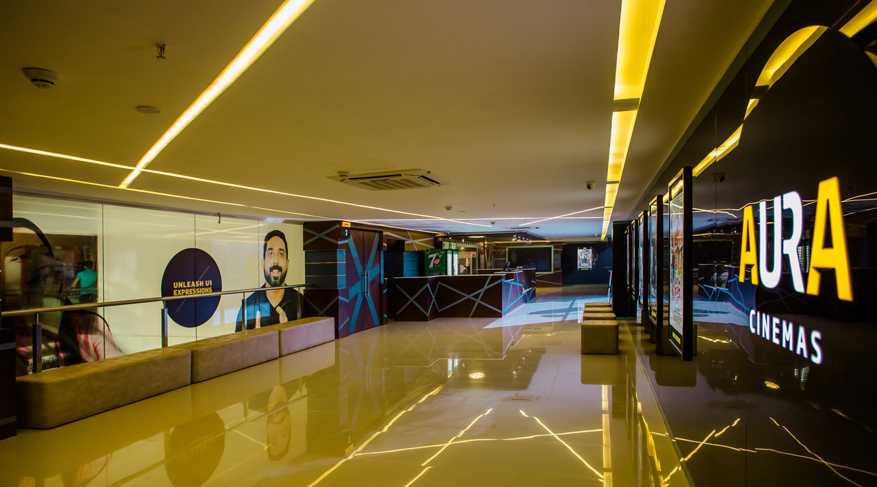 Aura Cinemas multiplex interior: View of the concession stand, glowing ceiling lights, and current movie posters, offering a welcoming atmosphere for moviegoers.