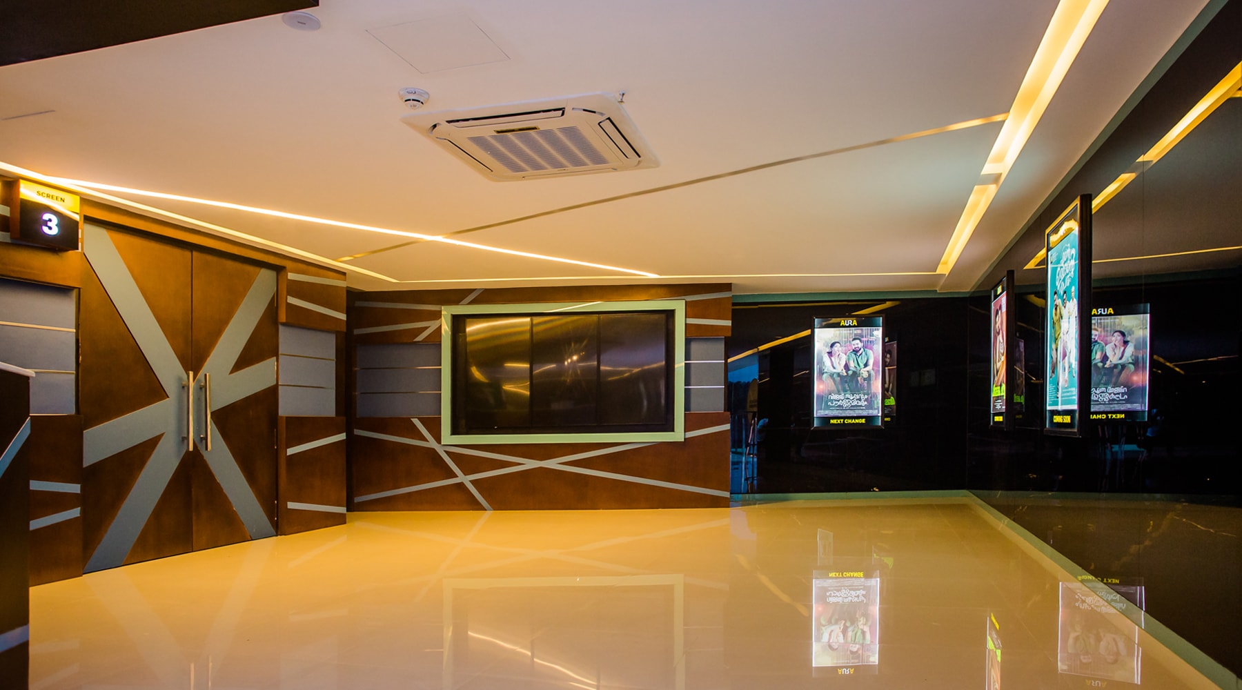 Aura Cinemas multiplex interior: View of the concession stand, glowing ceiling lights, and current movie posters, offering a welcoming atmosphere for moviegoers.