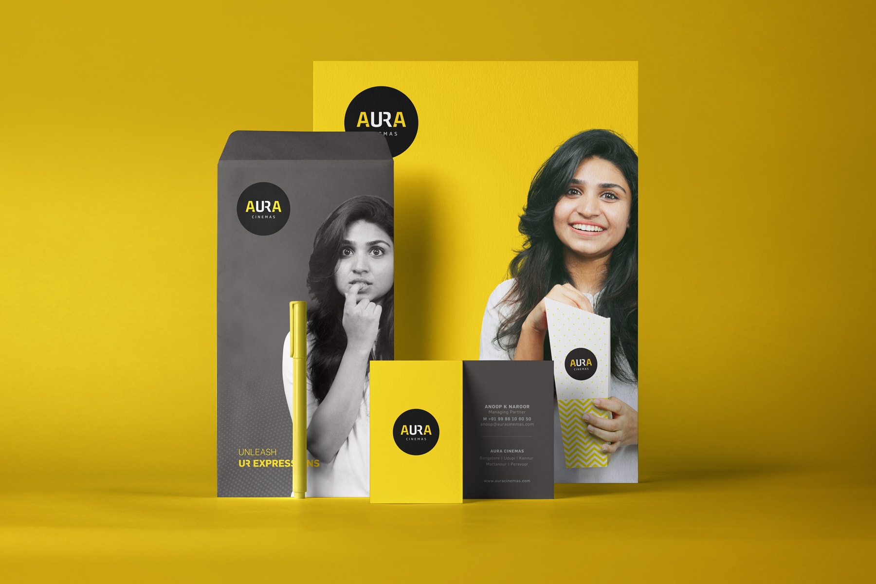 Various Aura Cinemas promotional items: yellow poster, black envelope, and popcorn container with the brand logo and a woman's image, perfect for cinema marketing in Bengaluru.