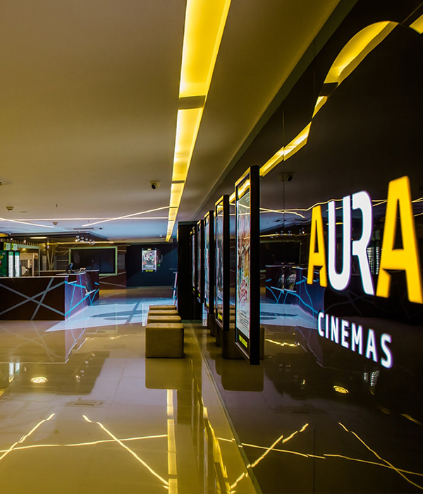 Modern and brightly lit interior of Aura Cinemas, showing a stylish lobby with seating, reflective floors, 
                and the prominent Aura Cinemas logo on the wall.