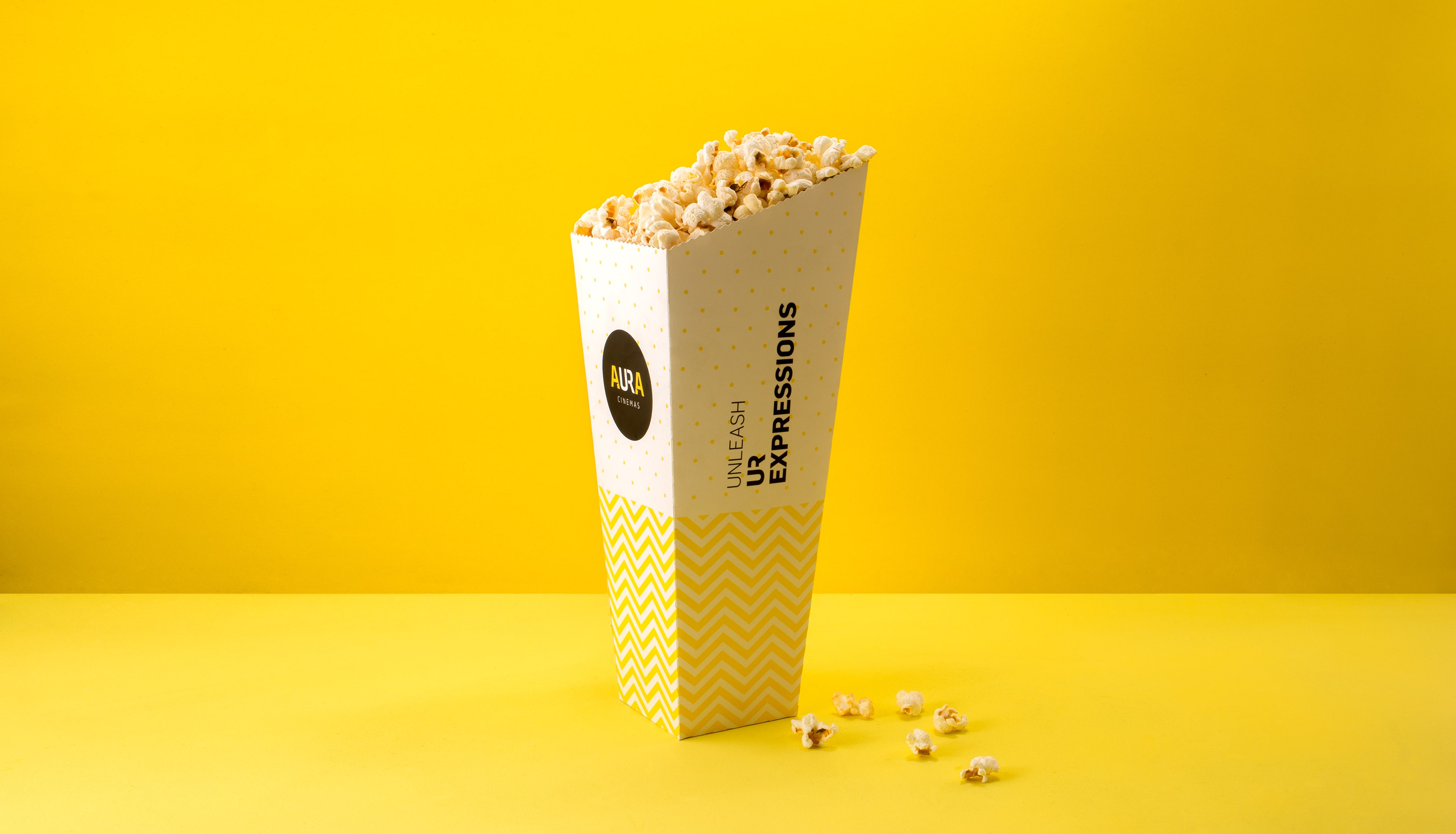 Aura Cinemas branded popcorn in a yellow zigzag-patterned container, offering a perfect cinema snack experience