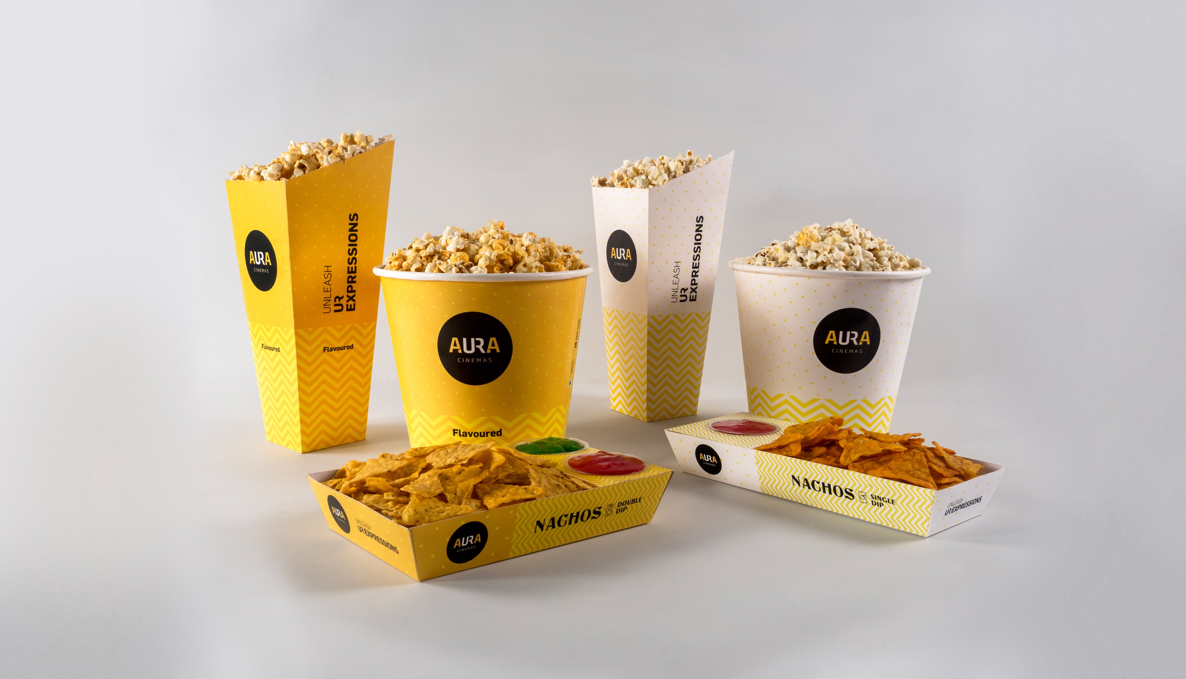 Aura Cinemas premium popcorn boxes, tubs, and nacho trays with yellow and white packaging design featuring brand colors and tagline Unleash Your Expressions