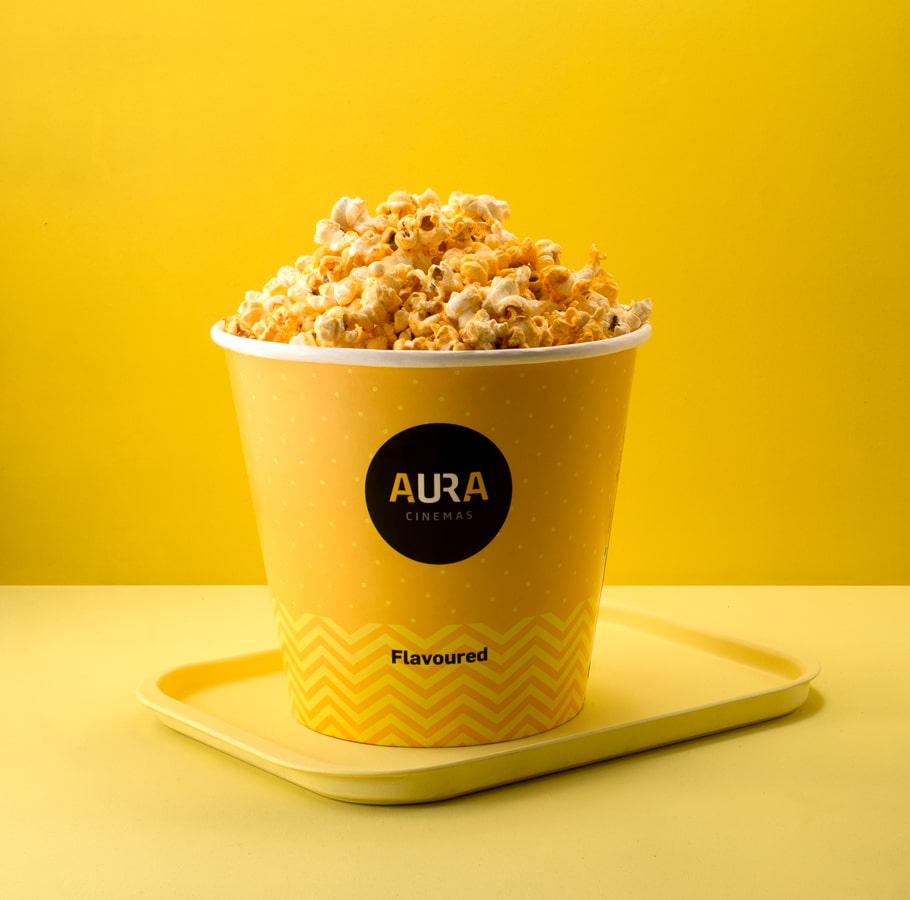 Aura Cinemas flavored popcorn in a yellow zigzag-patterned bucket on a tray, ideal for an enjoyable movie snack experience