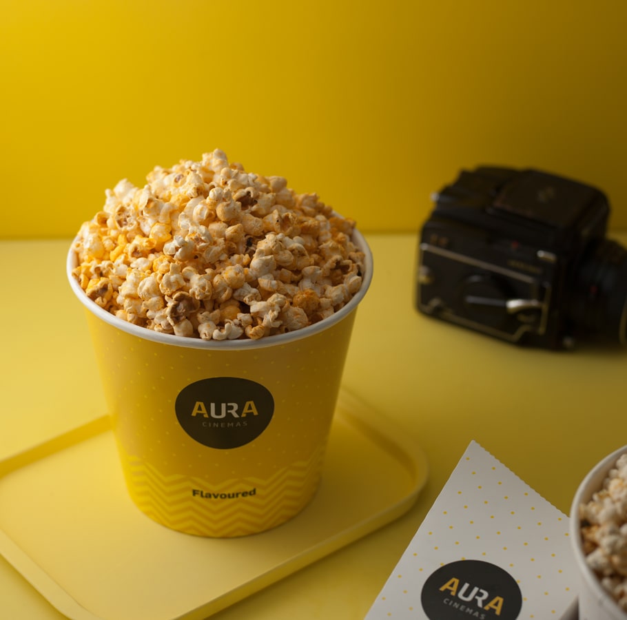 Aura Cinemas flavored popcorn in a yellow zigzag-patterned bucket with a tray, paired with a vintage camera for a classic cinema vibe