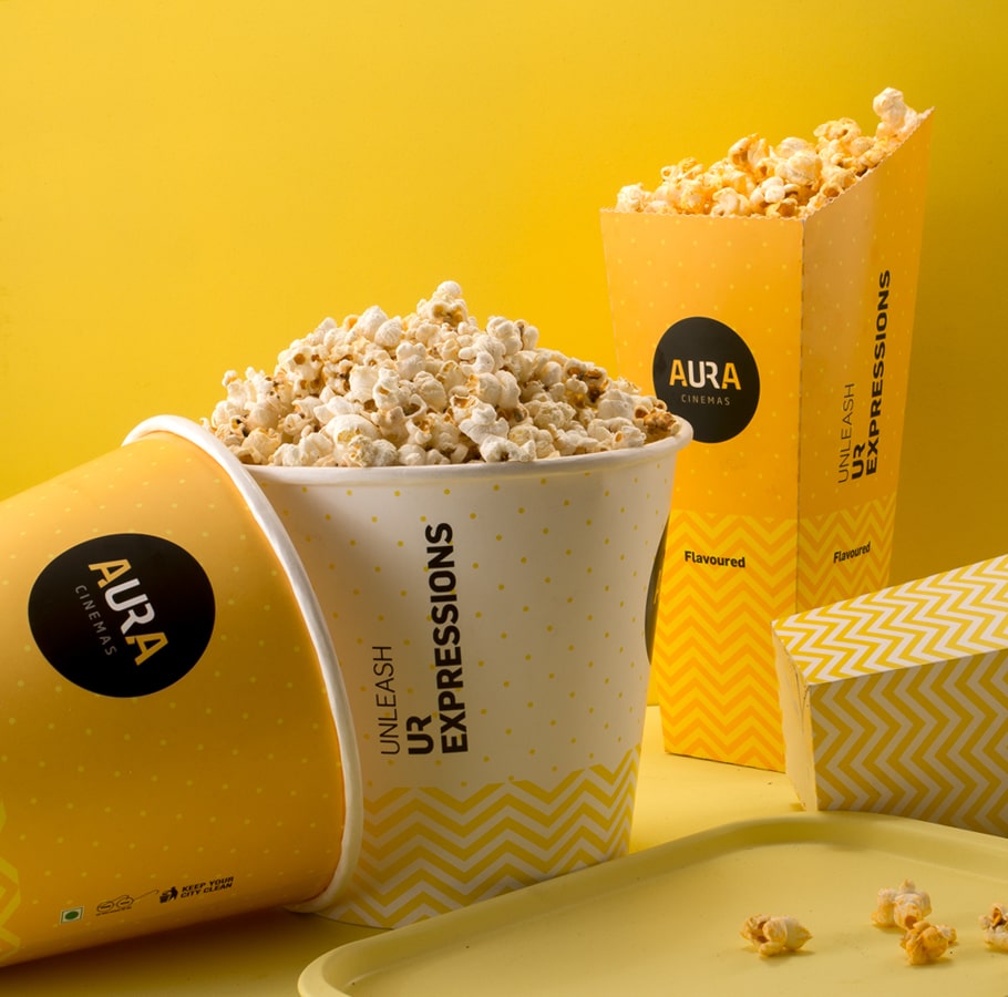 Aura Cinemas flavored popcorn in yellow zigzag-patterned buckets and containers, perfect for an enhanced movie snack experience