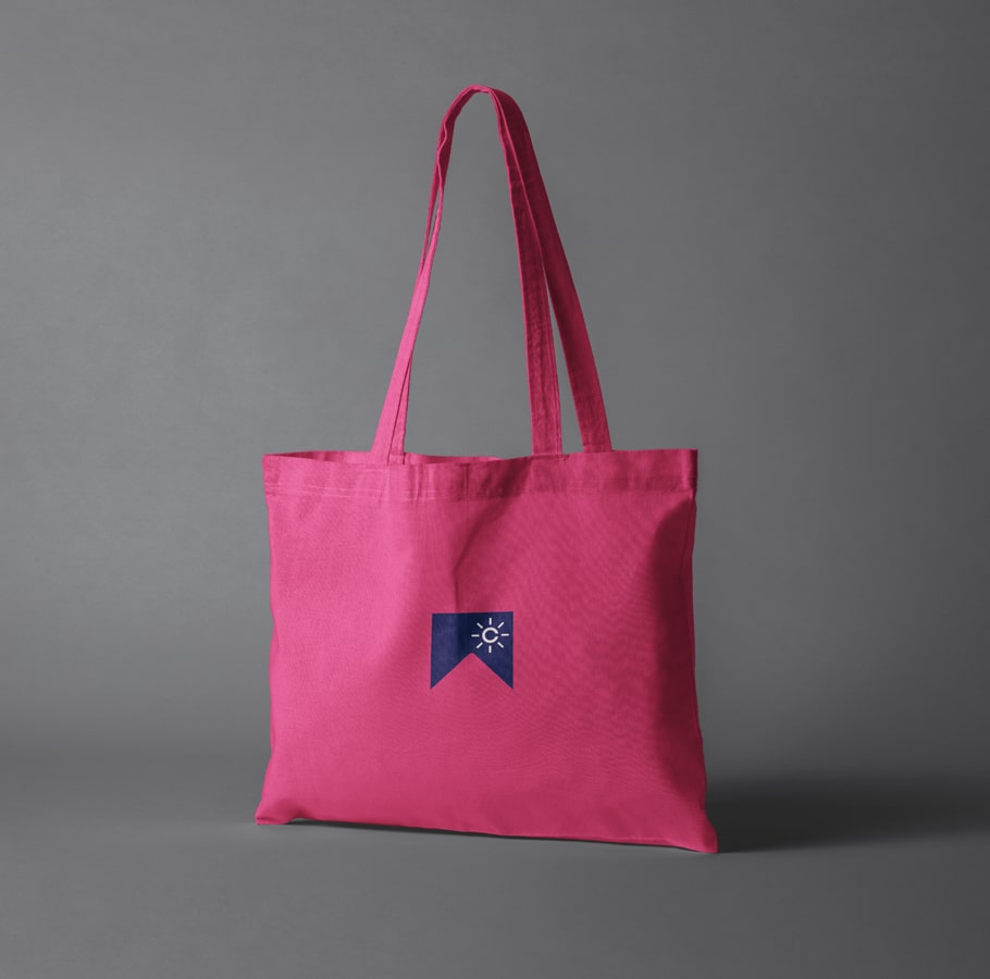 Club W pink tote bag with long handles and small blue emblem featuring white sun icon, minimalist design photographed against gray background