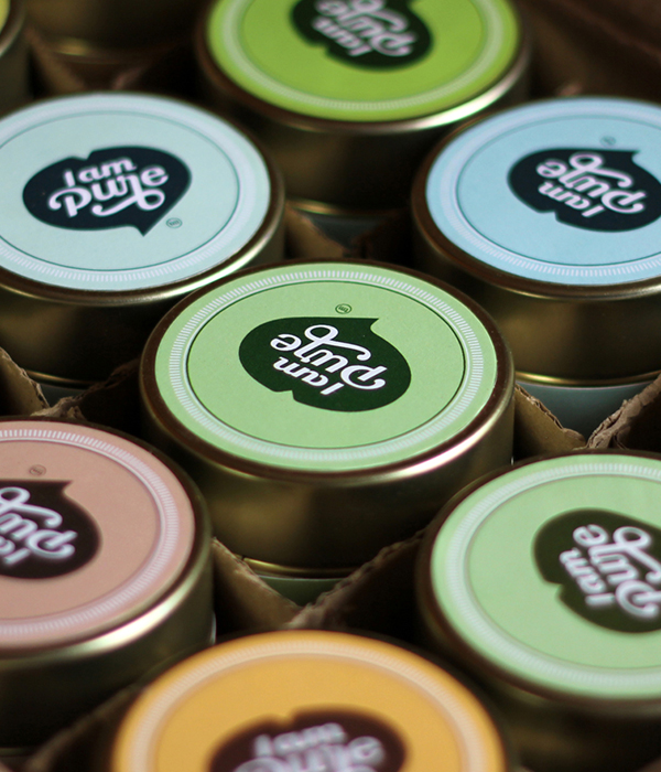 Close-up of a variety of 'I am Pure' branded tins, 
                featuring different pastel-colored lids with the logo, packaged neatly in a box.