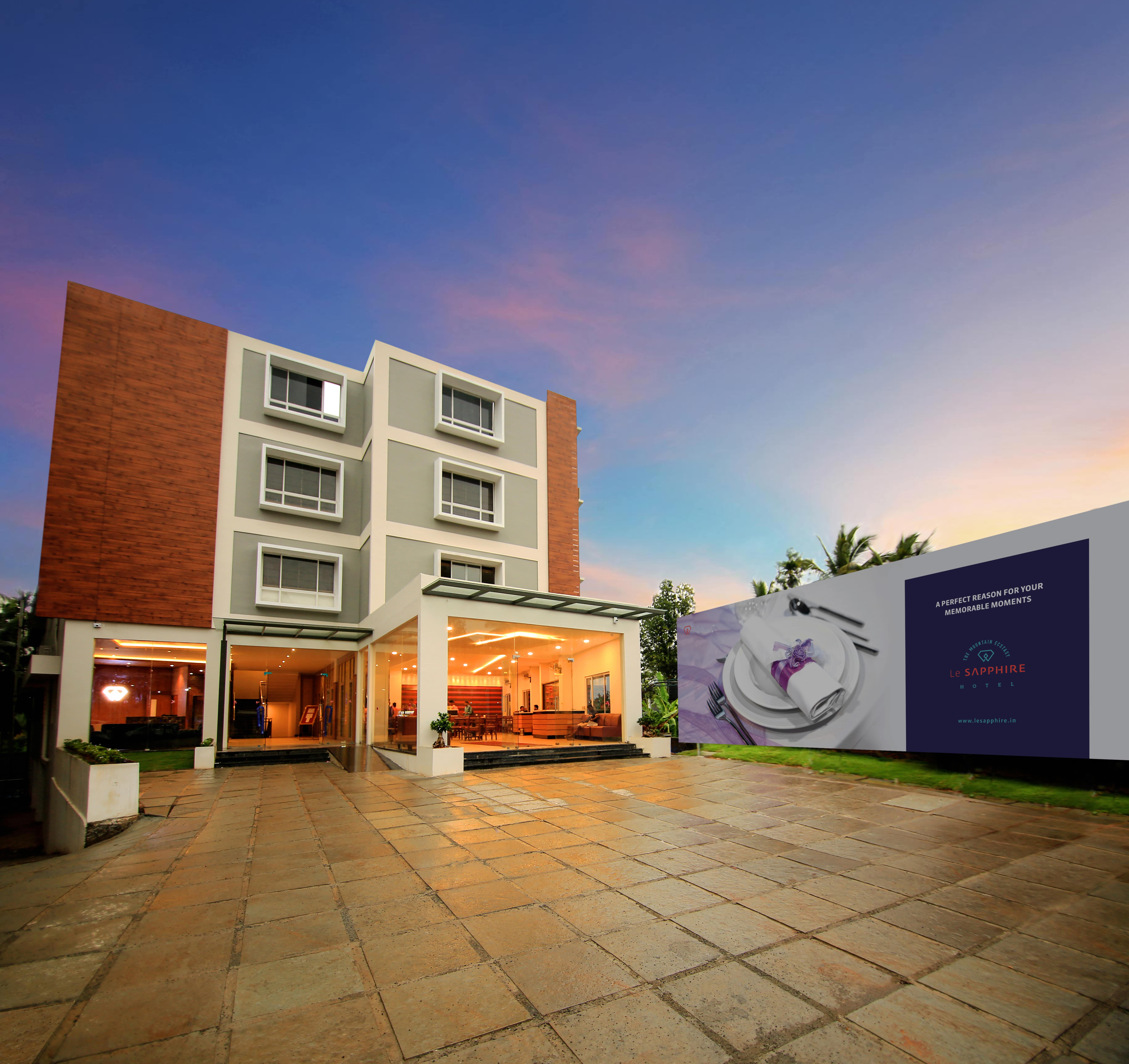 Le SAPPHIRE Hotel exterior at dusk, featuring its modern architecture, entrance, and a large outdoor sign with a dining setting, ideal for memorable moments.