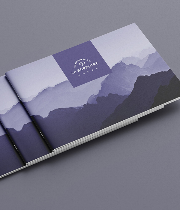 Close-up of a brochure for Le Sapphire Hotel, featuring a stylish design with layered, purple-toned mountain landscapes and the hotel's logo.
