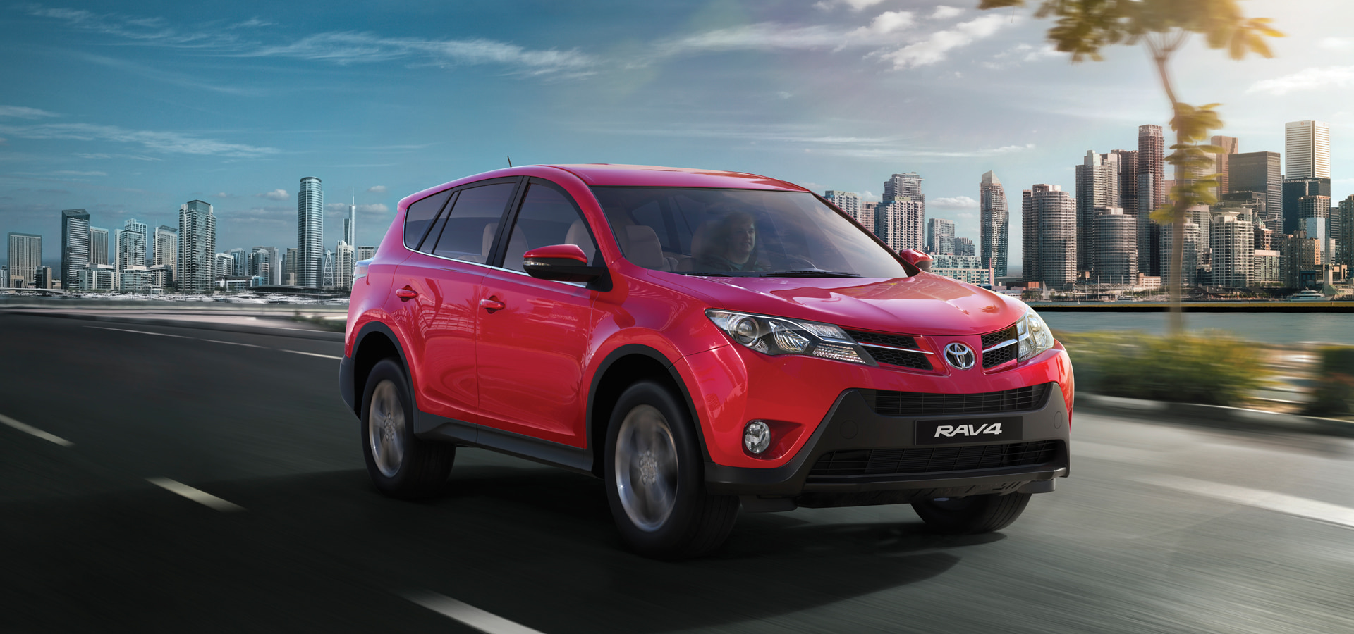 Nuetone vibrant red RAV4 SUV driving on a city road with a modern skyline and green trees in the background, showcasing the brand's dynamic lifestyle on the website
