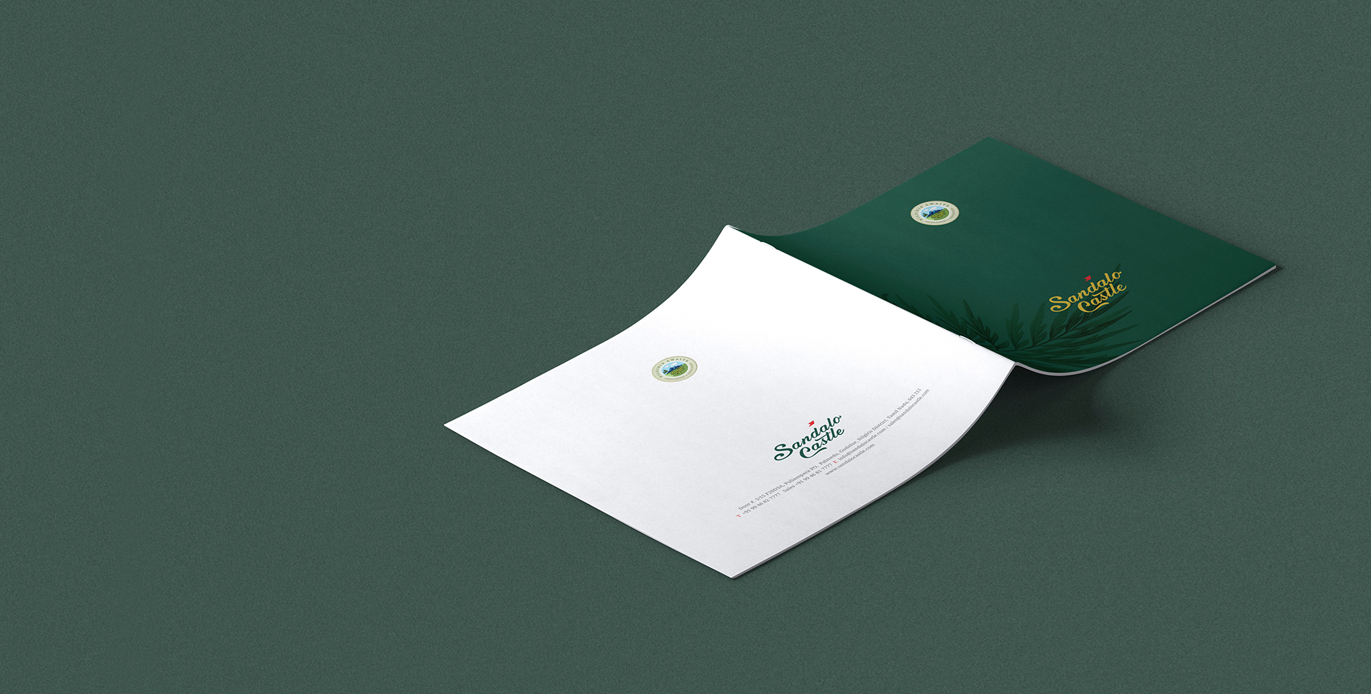 a high-angle shot of a white and green brochure or magazine for Sandalo Castle, with the front cover showing the brand's logo and name, lying open on a dark green surface.
