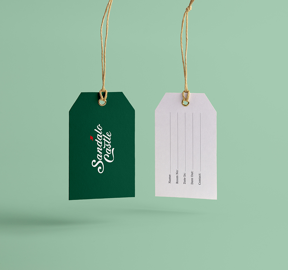 Two luggage or product tags for Sandalo Castle hang from a string against a mint green background. One tag is dark green with the brand logo in white, and the other is white with blank lines for information like 
