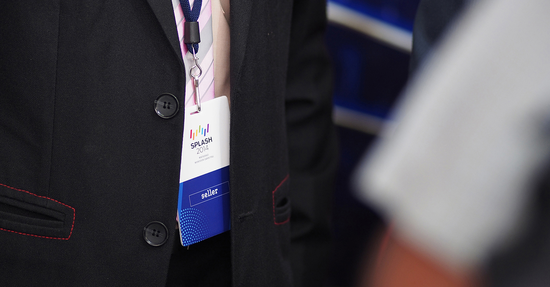 A close-up of a person wearing a black suit jacket, with a SPLASH 2014 badge and lanyard visible, identifying them as a seller at the event