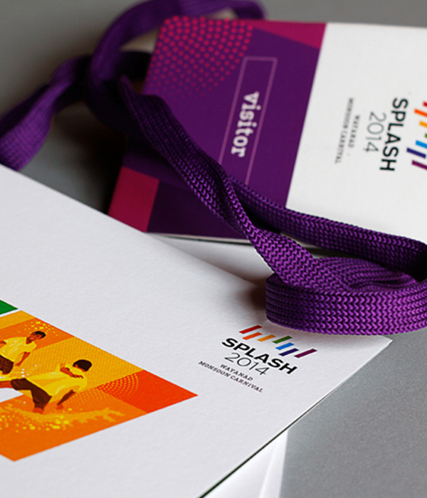 Close-up of a visitor badge and a brochure
                 for 'Splash 2014,' a monsoon carnival in Wayanad, 
                featuring a colorful design and a purple lanyard.