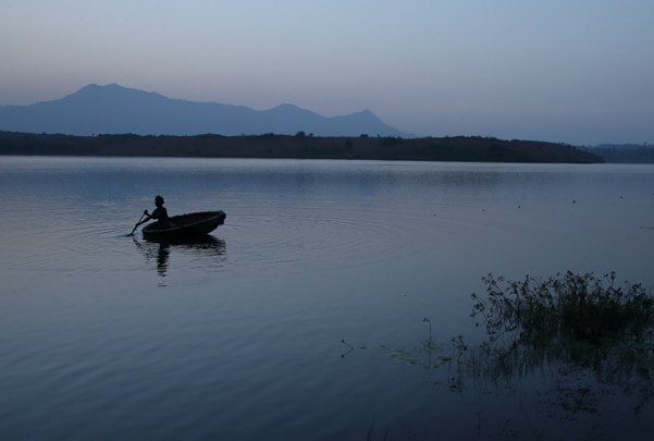 Silhouette of person rowing boat on tranquil Vistara lake during twilight with mountain backdrop reflecting natural serenity and peaceful retreat