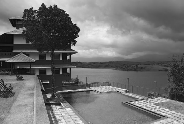 Vistara resort overlooking serene lake and mountains with swimming pool and lush greenery under cloudy sky