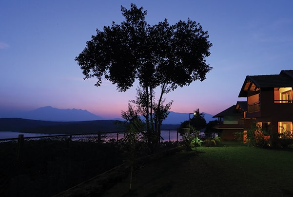 Vistara resort at dusk with silhouette tree, calm lake, and mountain backdrop creating peaceful natural retreat