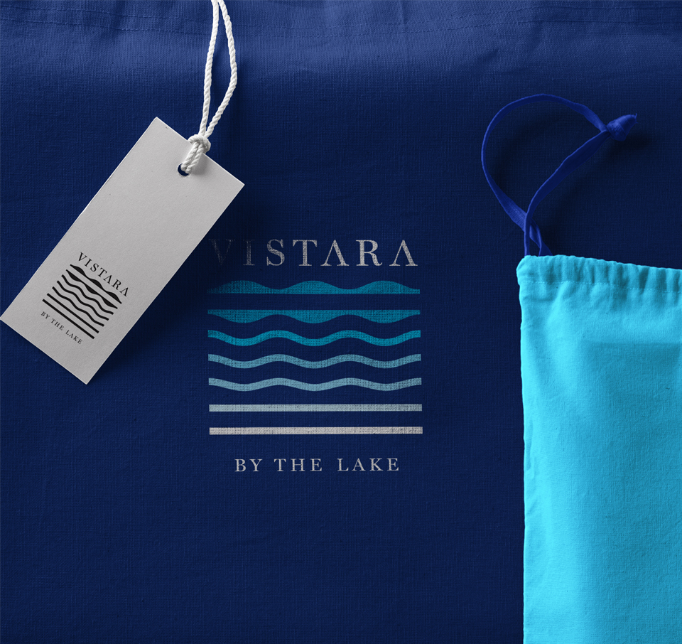 Vistara by the Lake logo with stylized blue waves on dark blue fabric and light blue drawstring bag showcasing resort branding and identity